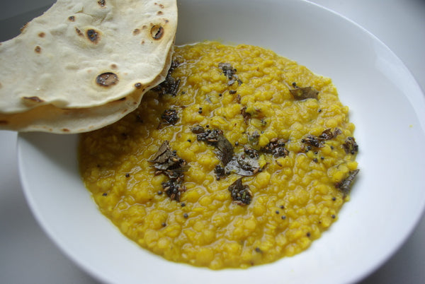 Red lentil daal with fried curry leaves and flatbread in a white bowl.