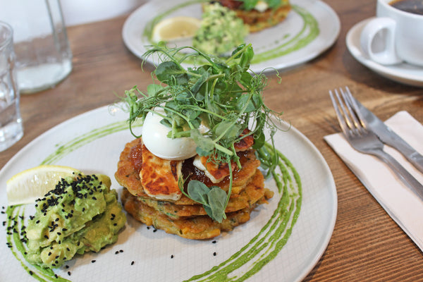 Our courgette and sweetcorn fritter dish: a stack of fritters topped with chilli jam, halloumi and a poached egg with avocado on the side.