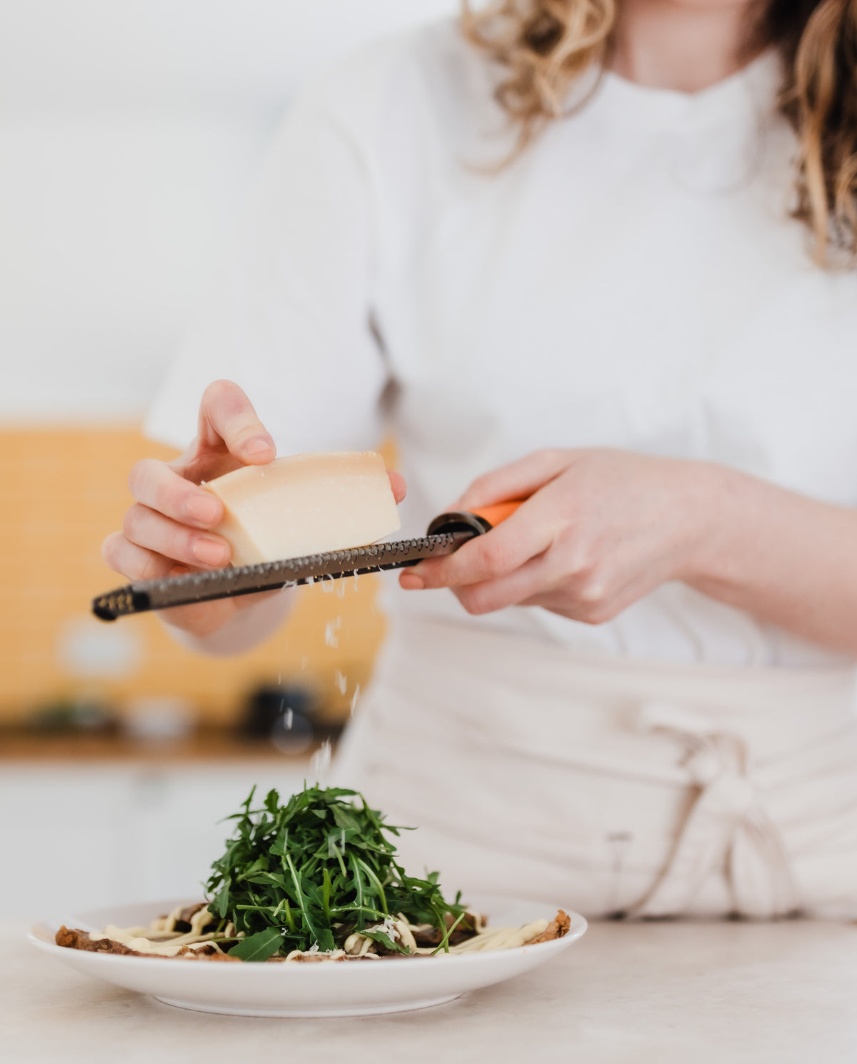 A female chef grating parmesan over a plate of roast beef and rocket.