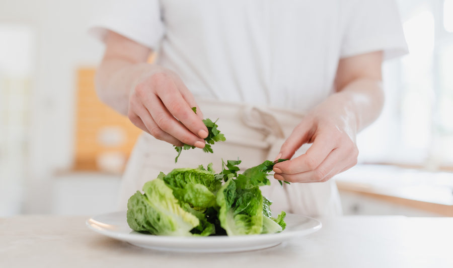 A chef in a white top placing herbs on top of gem lettuce on a white plate.