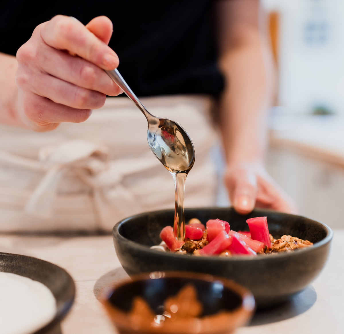 Honey dripping from a spoon over some rhubarb granola.