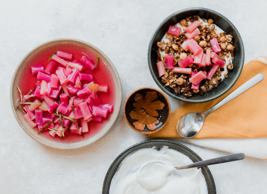 A flat lay of various bowls and spoons including poached rhubarb, yoghurt, honey and granola.