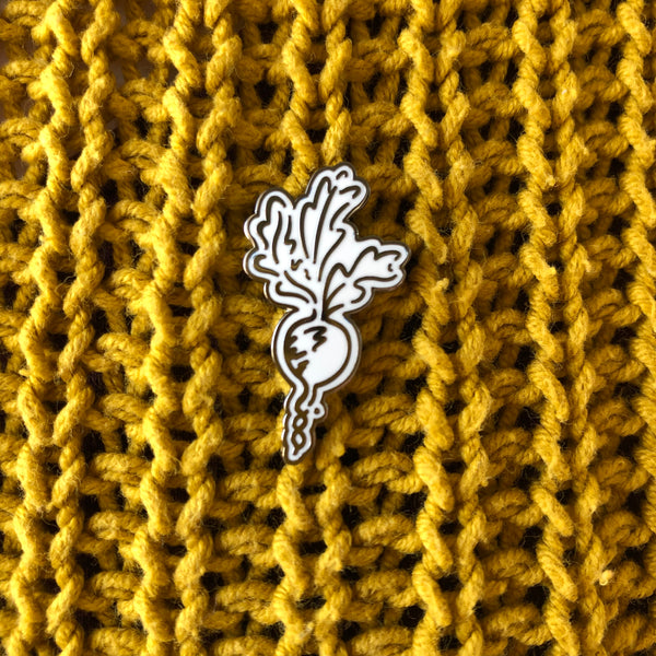 A black and white enamel radish pin on a mustard jumper.